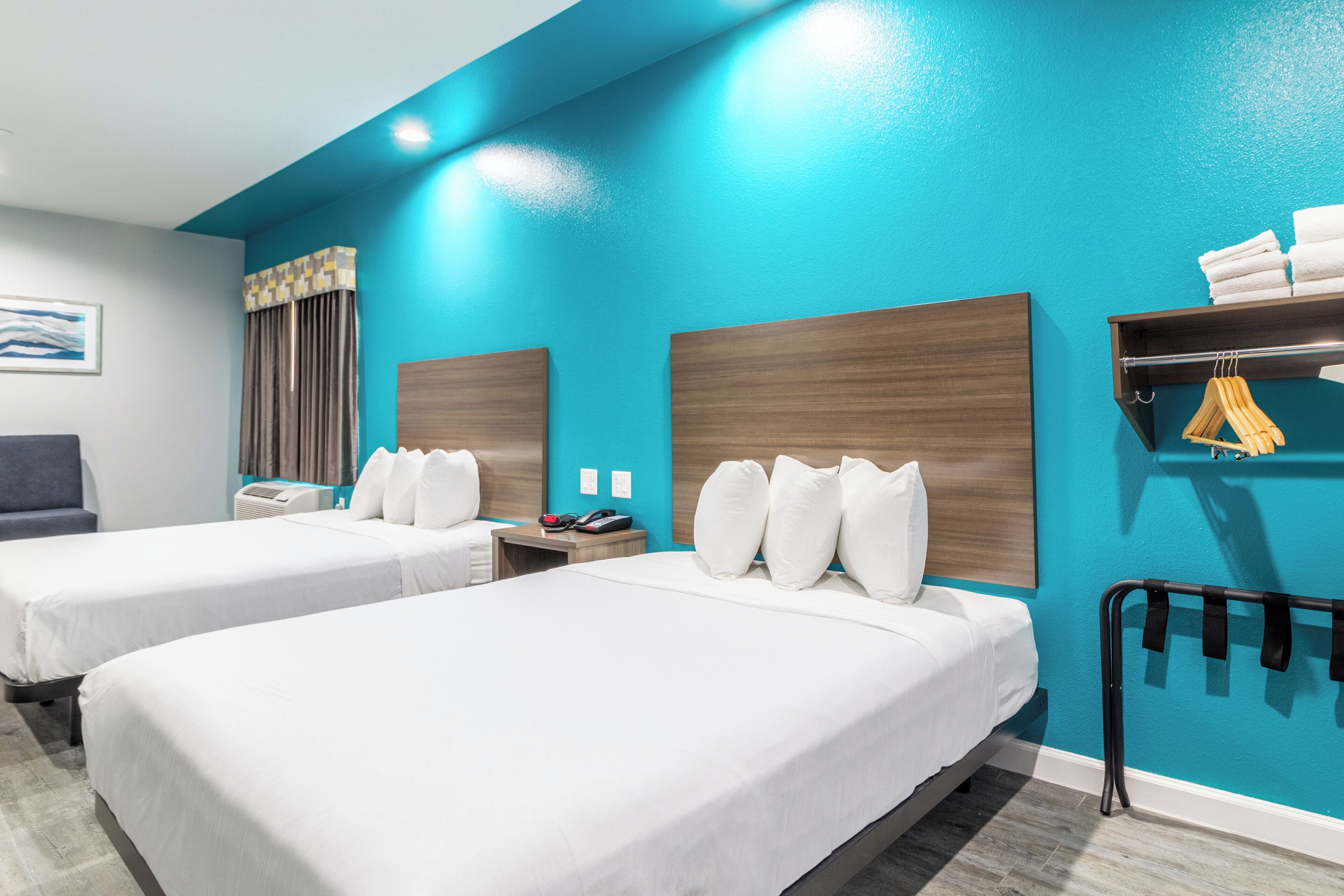 A hotel room with two beds, a desk, a chair, a coat rack, and a bathroom.