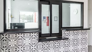 Un espace d’accueil avec un mur décoré de motifs, un bureau et une fenêtre donnant sur les bâtiments environnants.