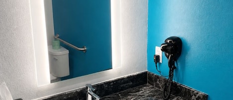 A bathroom with a white sink, black marble countertop, a blue wall, and a mirror with a light.