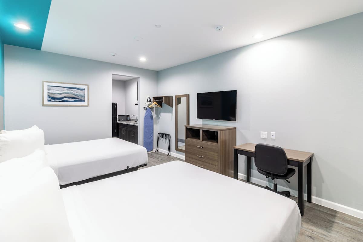 Ein Hotelzimmer mit zwei Betten, einem Schreibtisch, einem Stuhl, einem Fernseher und einem Kleiderschrank.