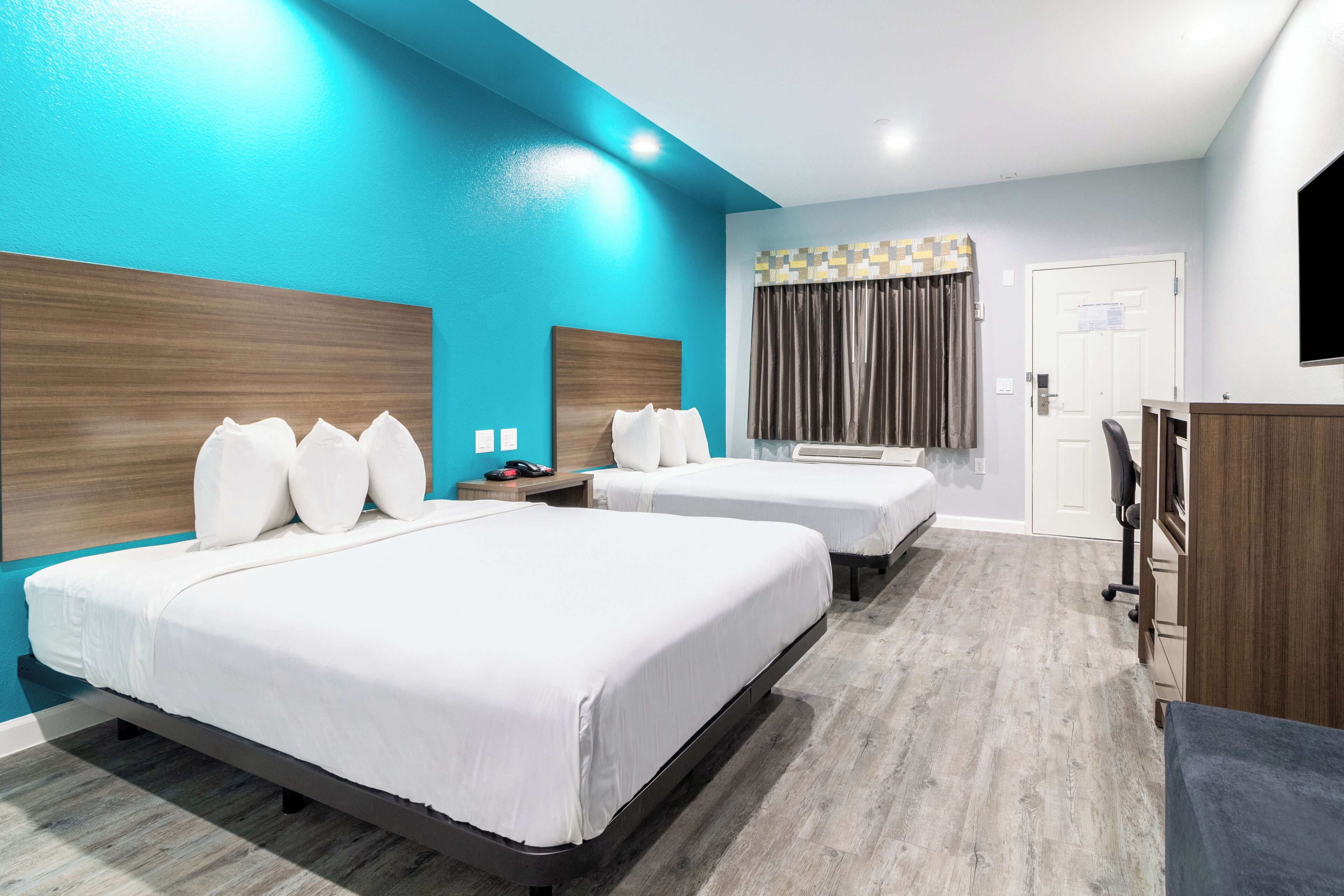 Habitación de hotel con dos camas, un escritorio, un televisor y una puerta.