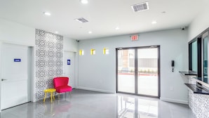 Un hall d’entrée propre et moderne, avec un comptoir d’accueil, un fauteuil rouge et un mur orné de motifs.
