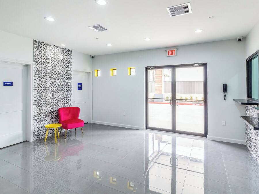 Un vestíbulo moderno y luminoso con mostrador de recepción, una silla roja y un muro con diseño.