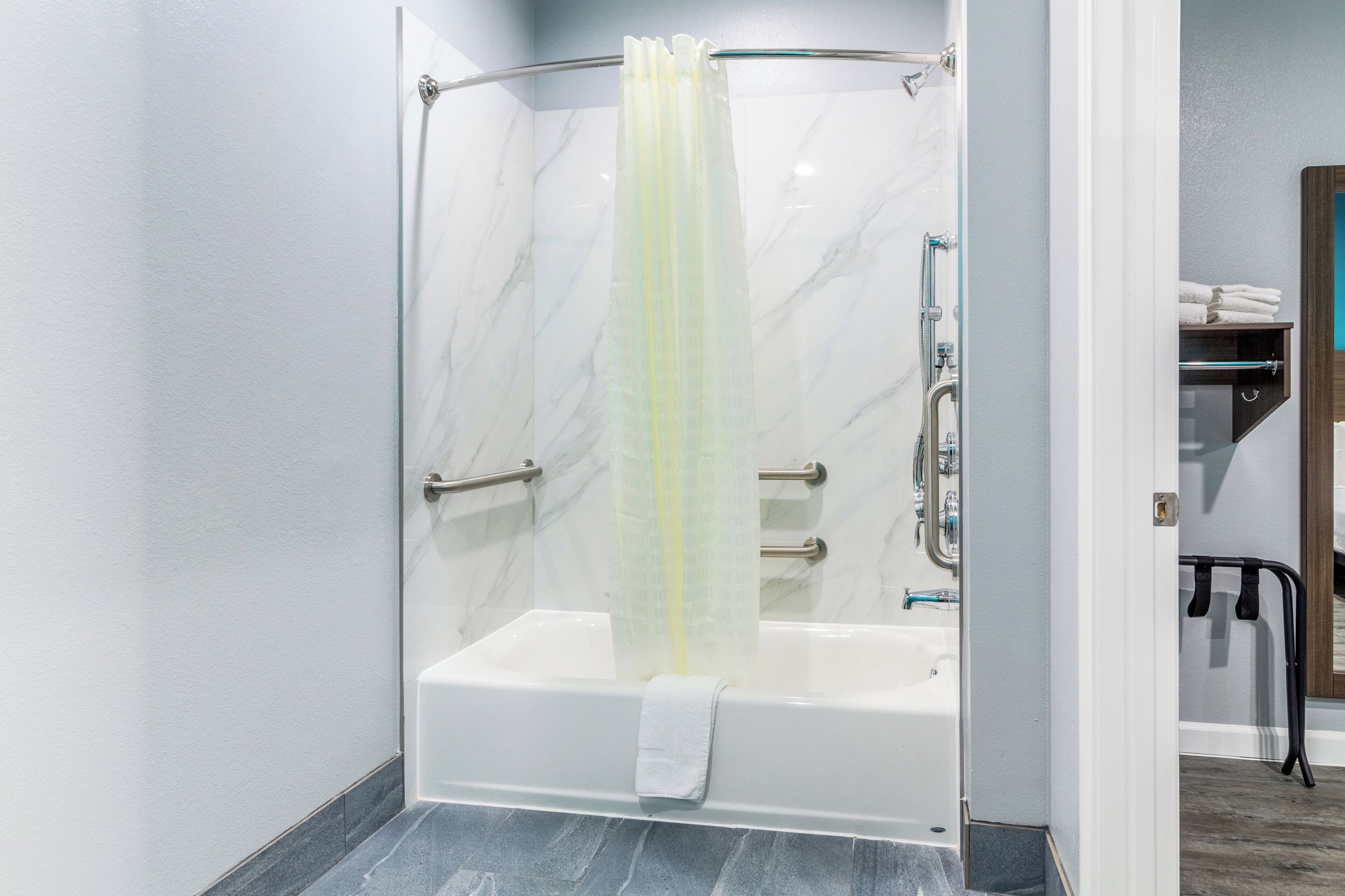 Une douche à l’italienne avec une porte en verre, un porte-serviettes et une barre d’appui.