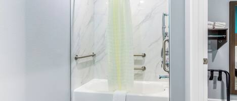 Une douche à l’italienne avec une porte en verre, un porte-serviettes et une barre d’appui.