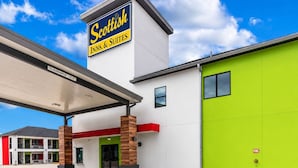 Un hôtel avec une enseigne bien visible indiquant « Scottish Inns & Suites », une entrée abritée et une porte latérale d’un vert vif.