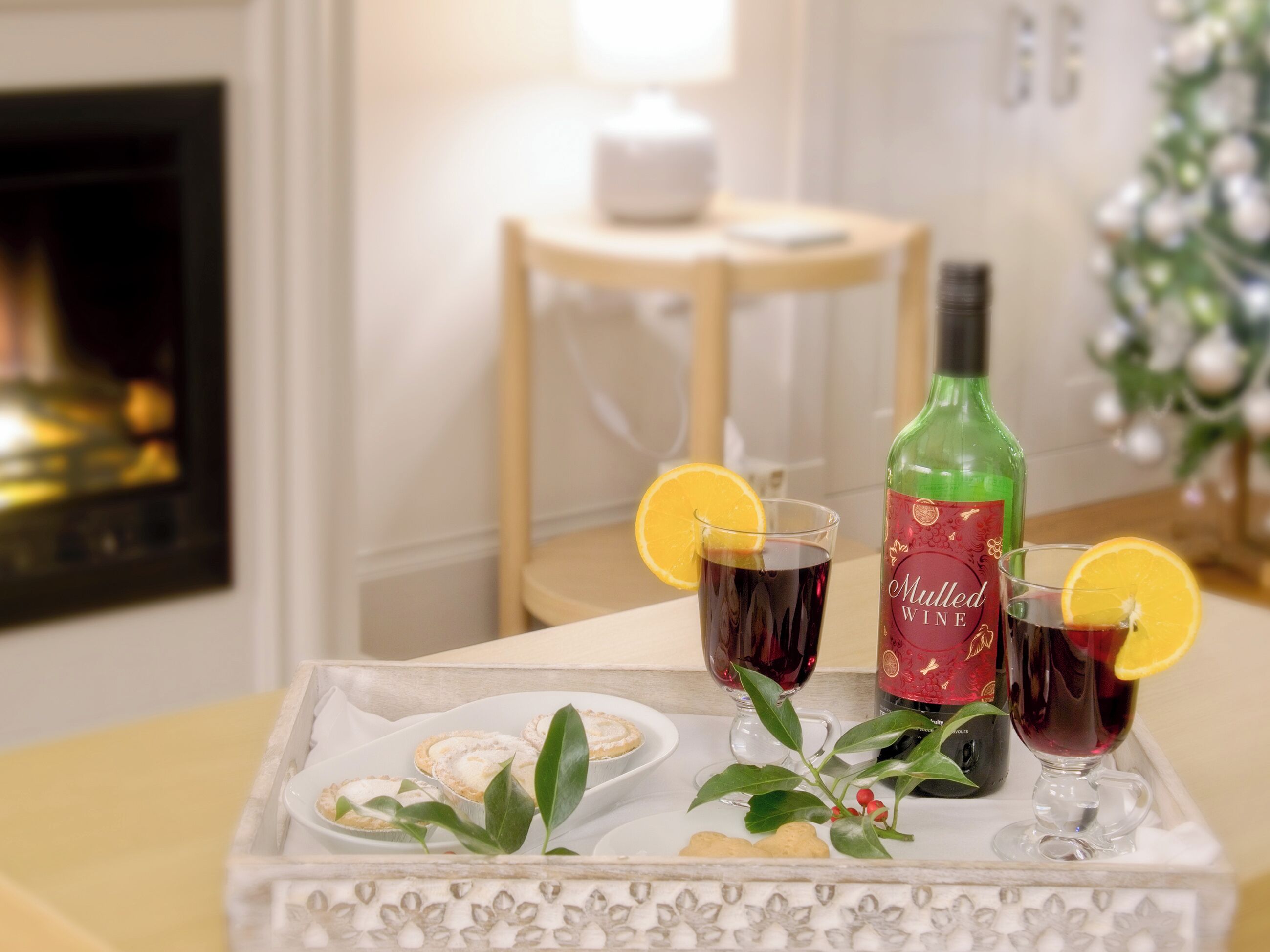 Un plateau avec deux verres de vin chaud, une bouteille de vin chaud et une assiette de pâtisseries.