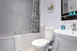A bathroom with a toilet, a bathtub, a shower curtain, a sink, and a mirror.