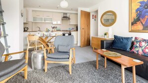 A modern living room with a sofa, a coffee table, and a dining area with chairs and a table. - Sunnyside - Apartment Moments from Poole Quay (Poole)