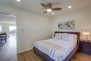A bedroom with a bed, a ceiling fan, a nightstand, a lamp, and a painting on the wall.