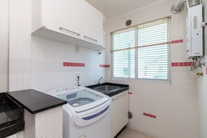 Eine kleine Küche mit Waschmaschine, Spüle und einem Fenster mit Jalousien.