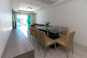 Een moderne eethoek met een glazen tafel, beige stoelen en een vaas met bloemen.
