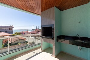 Un balcon donnant sur des immeubles et sur une enseigne de restaurant, une cheminée recouverte de carreaux et un comptoir de cuisine avec un évier.