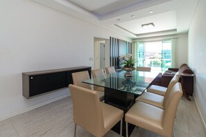 Een moderne eetruimte met een glazen tafel, beige stoelen, een donkere console en uitzicht door een glazen deur.