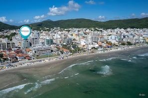 A coastal cityscape with a beach, buildings, and mountains in the background.