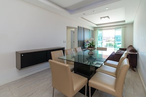 Un espace repas moderne avec une table en verre, des chaises de couleur beige, une console sombre et une vue à travers une porte vitrée.