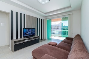 Una sala de estar moderna con un televisor de pantalla plana, un sofá y un ventanal corredero que da a un balcón.