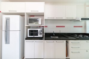 Une cuisine avec des meubles blancs, un four à micro-ondes, un réfrigérateur et une cuisinière à gaz.