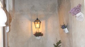 Un espacio al aire libre acogedor, con una mesa y sillas de metal, un farol colgante y plantas en macetas.