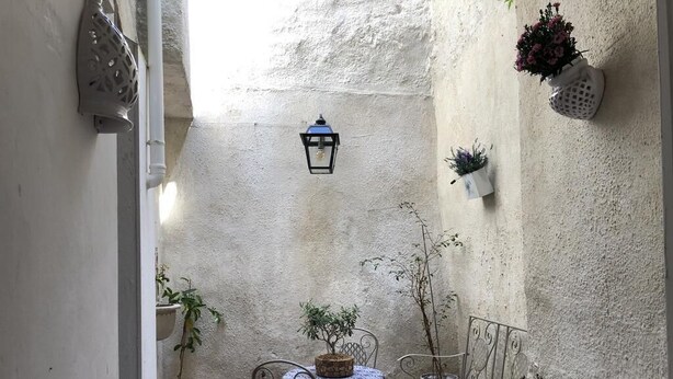 Un pequeño patio al aire libre con una mesa, sillas, plantas en macetas y un farol en la pared.
