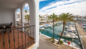 Un balcón con vista a un puerto deportivo, palmeras y edificios al fondo.