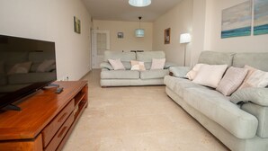 Una sala de estar con un televisor sobre una mesa de madera, dos sofás con cojines, una lámpara y un cuadro en la pared.