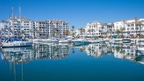 A marina with multiple boats docked, surrounded by white buildings with balconies and palm trees. - Marina de la Duquesa 904 (Manilva)