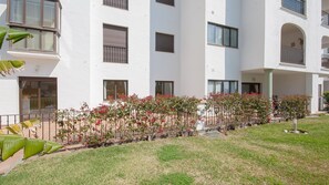Un edificio de varios pisos con balcones, un área de estar al aire libre techada y un jardín con plantas en flor.