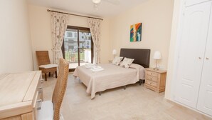 A bedroom with a bed, a chair, a desk, a nightstand, and a door. - Marina de la Duquesa 904 (Manilva)