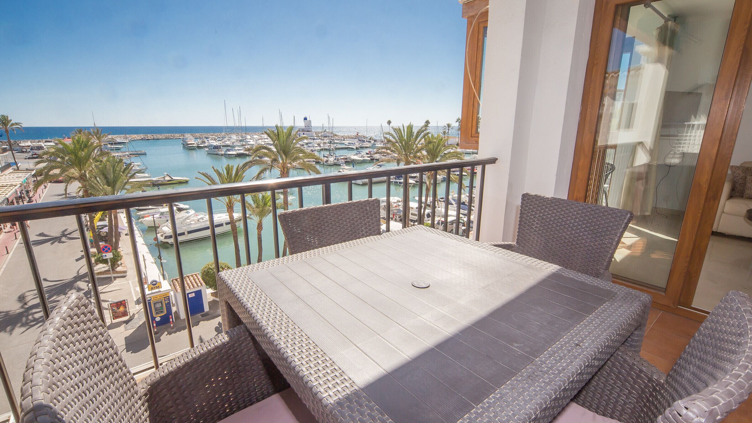 A balcony with wicker furniture, overlooking a marina with boats and a clear blue sky.