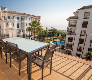 Un balcon avec une table et des chaises, donnant sur une piscine et des immeubles.