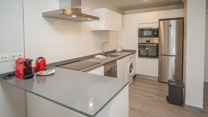 Ett modernt kök med ett kylskåp i rostfritt stål, en inbyggd ugn, en mikrovågsugn och en tvättmaskin.