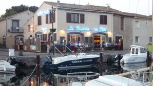 A waterfront restaurant with outdoor seating, boats docked nearby, and a building with a sign reading "La Tavernia du Pescatore". - Sunny apartment overlooking Etang de Thau (5 km from the sea) (marseillan)
