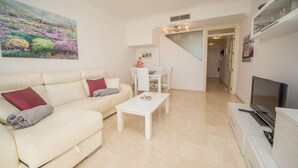 Ein Wohnzimmer mit einer Couch, einem Couchtisch und einem Fernseher. Eine Treppe führt in einen anderen Raum.