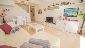 Ein modernes Wohnzimmer mit Sofa, Couchtisch, Fernseher und einem Essbereich mit Stühlen.