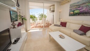 Ein modernes Wohnzimmer mit einem beigefarbenen Sofa, einem Couchtisch und einem Fernseher. Es gibt einen Balkon mit einem weißen Stuhl und einem Tisch.
