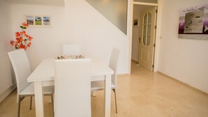 Ein Essbereich mit einem weißen Tisch und Stühlen, einer Blumenvase und einer Treppe, die in einen anderen Raum führt.