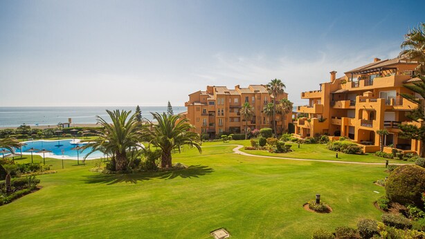 Ein Resort mit Swimmingpool, gepflegter Rasenfläche und Blick auf den Strand.
