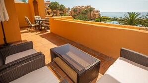 Ein Balkon mit Korbmöbeln, einem Tisch und Blick auf das Meer und Gebäude.