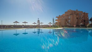 Une piscine d’un bleu éclatant, agrémentée de parasols, avec un bâtiment en arrière-plan.