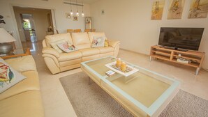 Ein Wohnzimmer mit einem beigen Sofa, einem Glastisch, einer TV-Konsole und Kunstwerken an der Wand.