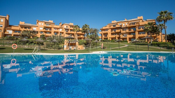 Un complexe hôtelier doté d’une piscine, de palmiers et d’immeubles à plusieurs étages avec des balcons.