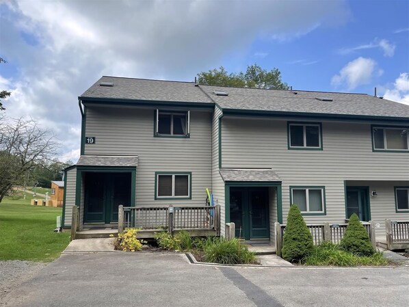 A two-story residential building with a green door and windows, a small porch area, and a number '19' sign.