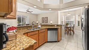 A kitchen with granite countertops, wooden cabinets, a dishwasher, and a dining area with a table and chairs.
