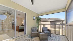 A balcony with wicker furniture, a clock, and a view of a house.