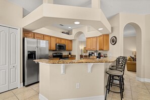 A kitchen with granite countertops, stainless steel appliances, wooden cabinets, and a central island with bar stools. - 537 Large 4BR Pool/Spa Conservation Views.2 Masters.Near Disney (Davenport)