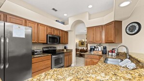 A kitchen with granite countertops, wooden cabinets, stainless steel appliances, and a clock on the wall.