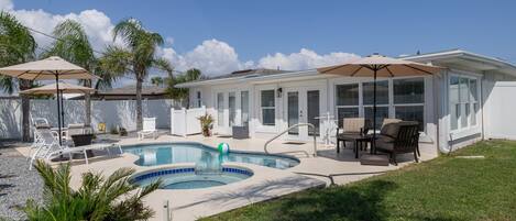 A backyard with a swimming pool, outdoor furniture, and palm trees.