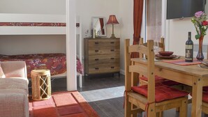 Una habitación pequeña con literas, cómoda de madera, mesa de comedor y televisor.