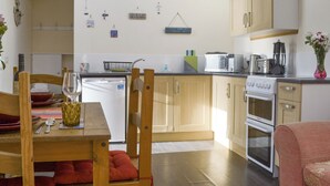 Una cocina compacta con armarios de madera, lavavajillas, microondas, estufa y un comedor con mesa y sillas.